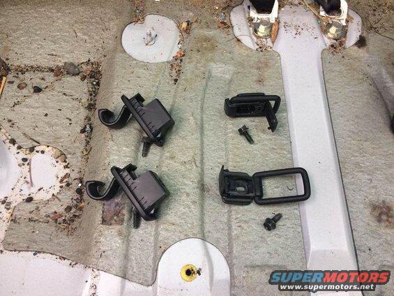 Two black seatbelt buckle receivers and two metal loops with screws on a vehicle floor.