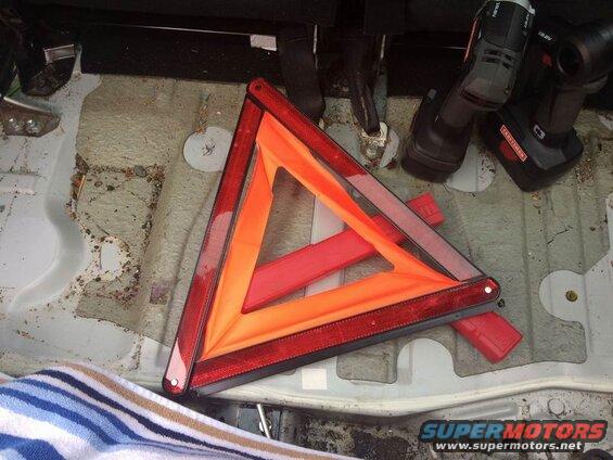 Reflective triangle warning sign and two cordless drills in a vehicle's cargo area.