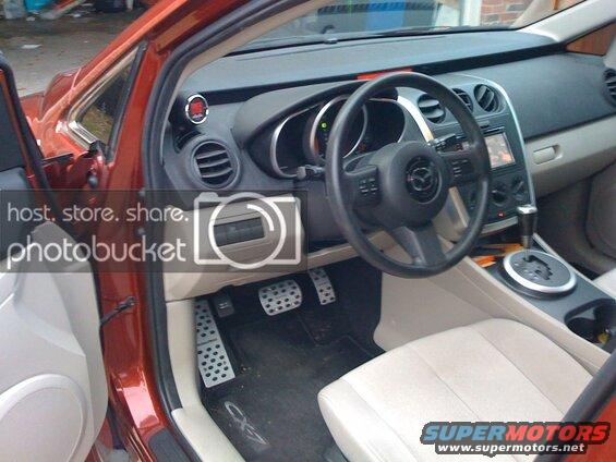 Interior of a red Mazda CX-9 with tan seats, black steering wheel, and aftermarket pedals.