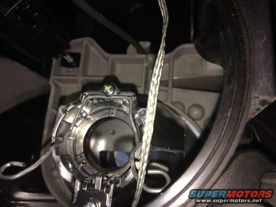Headlight bulb retainer clip secured by a screw in a gray plastic housing.