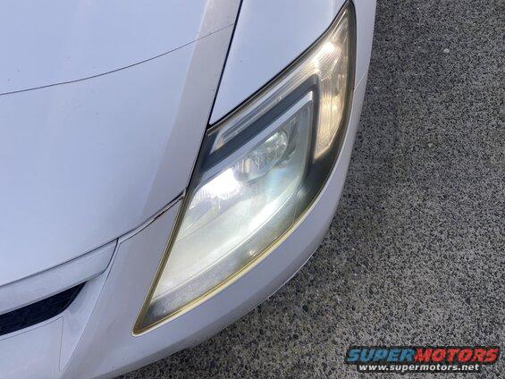 White vehicle's illuminated passenger-side headlight with golden trim.