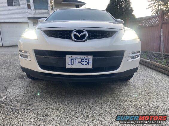 White Mazda CX-9 SUV front view with headlights on, showing license plate JD1 55H.