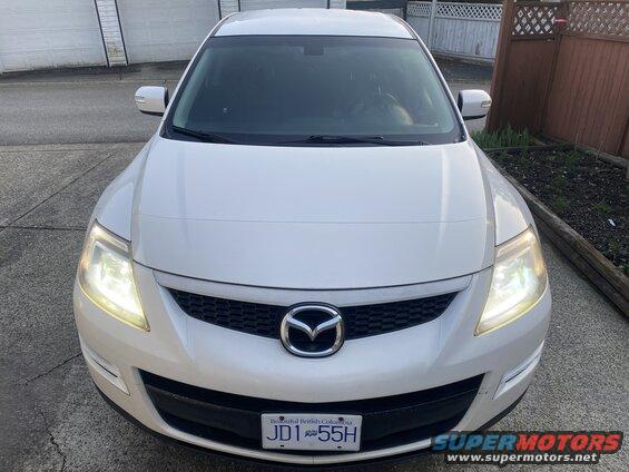 White 2009 Mazda CX-9 front view, headlights on, parked on driveway.