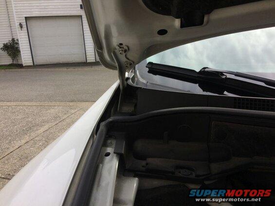 White car hood open, showing hinges and engine bay. Garage and driveway in background.