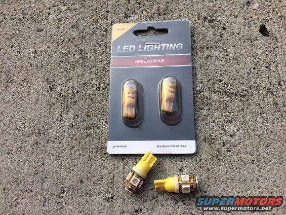 Package of amber LED bulbs next to two individual amber LED bulbs on concrete.