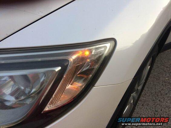 White vehicle's front passenger side headlight with amber turn signal lit.