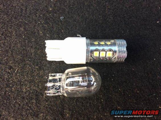 Incandescent automotive bulb next to an LED automotive bulb on a dark surface.