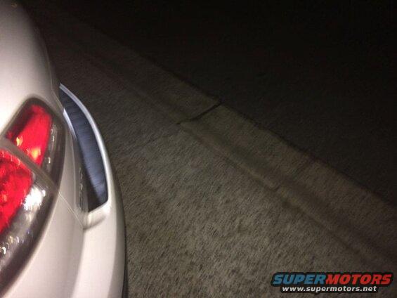 White SUV's rear quarter panel and taillight at night, parked next to a curb.
