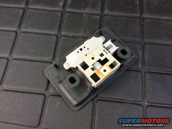 Disassembled interior light fixture with black and beige plastic components on a black textured surface.