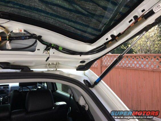 Open rear hatch of a white SUV showing wiring and gas strut.