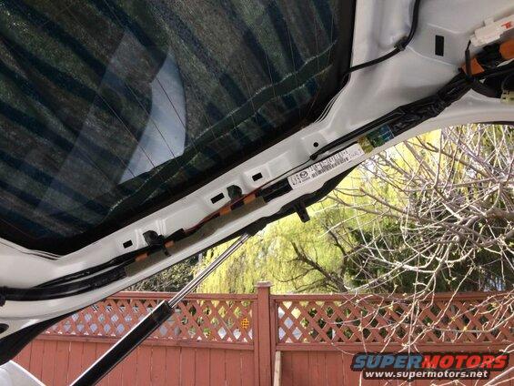 Interior of rear hatch of white vehicle, liftgate strut visible, sticker with barcode.