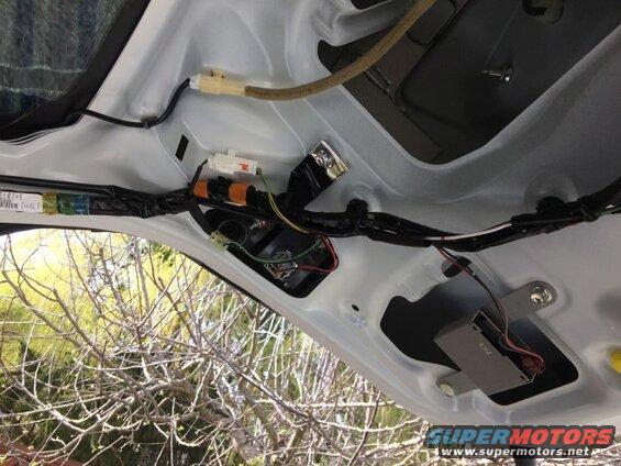 Underside of a car trunk lid showing wiring, connectors, fuse box, and electronic module.