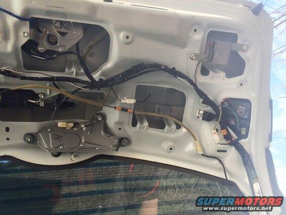 Interior of a white vehicle tailgate with wiring, electrical components, and wiper motor.