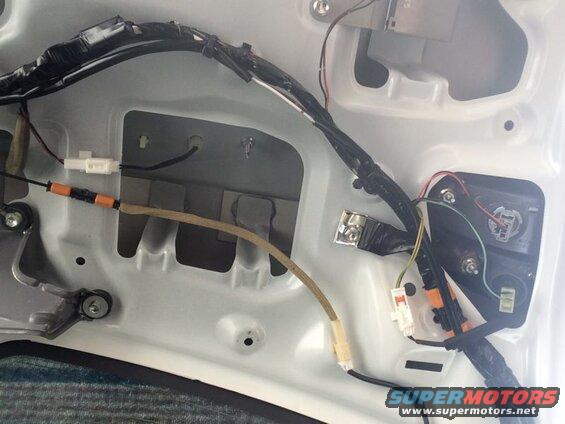 Wiring and connectors inside the trunk of a white vehicle, near the taillight assembly.
