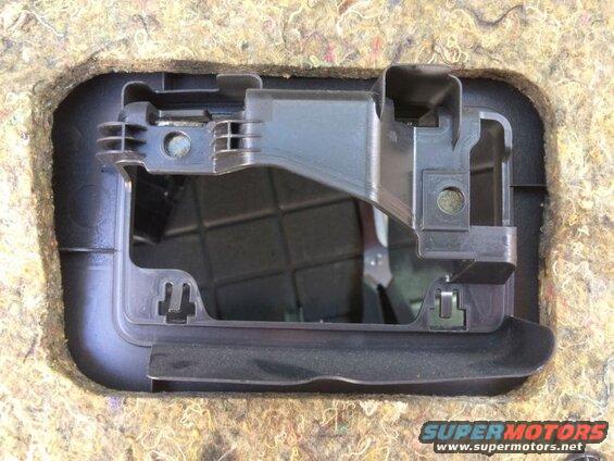 Black plastic bracket assembly inside a cutout of beige sound-dampening material.