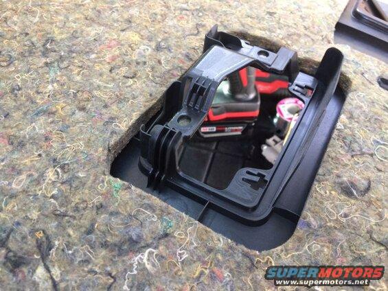 Black plastic trim piece installed over sound deadening material in vehicle interior with drill behind.