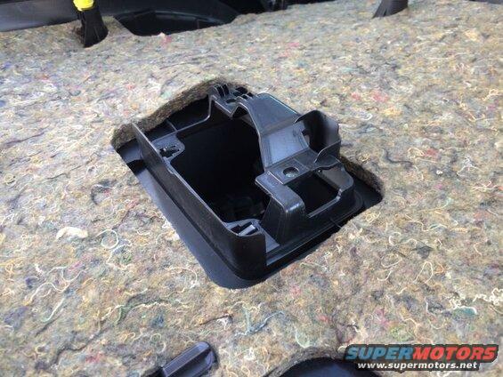 Black plastic bracket in vehicle floor sound dampening material