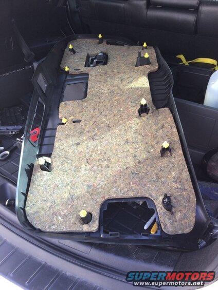 Interior trim panel with sound deadening material and yellow clips, laid out in a vehicle cargo area.
