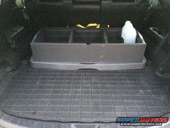 Cargo area of a dark SUV with a black organizer and a white jug on a rubber mat.