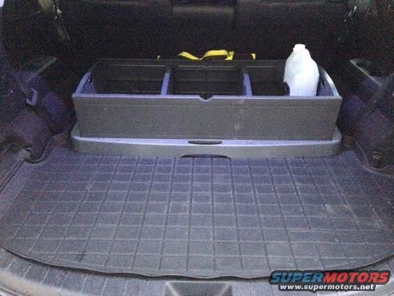 Cargo area of a dark SUV with a rubber mat and a three-compartment organizer holding a plastic jug.