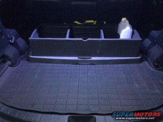 Cargo area of an SUV with black rubber floor mat and organizer holding a jug.