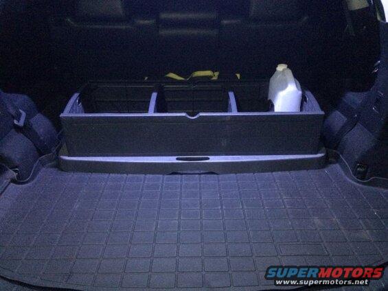 Black cargo organizer and jug in the trunk of a dark SUV with a rubber floor mat.