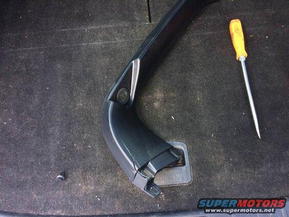 Black plastic car interior trim piece and a yellow screwdriver on dark carpet.