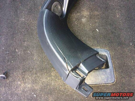 Cracked black plastic trim piece on vehicle floor carpet with detached fastener.
