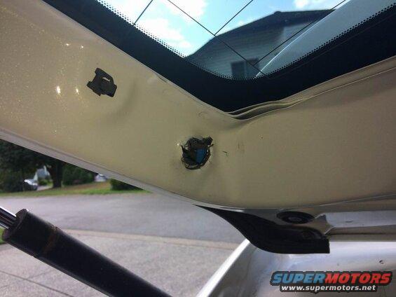 Interior of a white vehicle's rear hatch showing damage near the rear window and a gas strut.