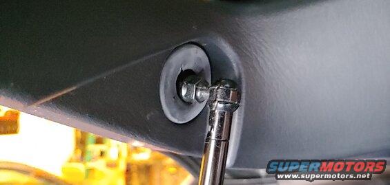 Socket wrench tightening a bolt on a dark gray car interior panel with a rubber grommet.