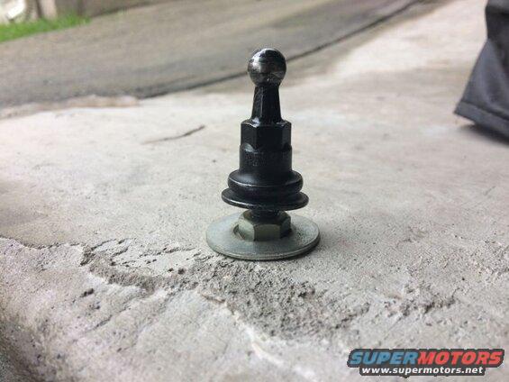 Black shift knob with spherical top on threaded shaft with nut and washer, on concrete.