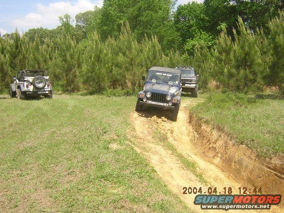 Blue Jeep Wrangler on a dirt trail with another Jeep and SUV in background