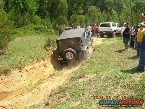 Jeep Wrangler driving through a dirt ditch with other vehicles and people watching
