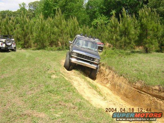 Dark SUV with off-road tires driving down a dirt trench, front grille visible