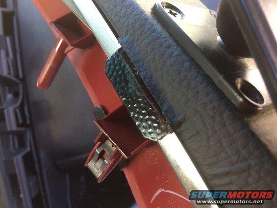 Close-up of red interior car part with metal clip and black textured trim.