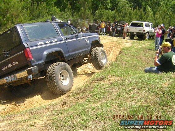 Dark blue off-road SUV climbing a dirt hill, other SUVs and people watching. Date stamp 2004