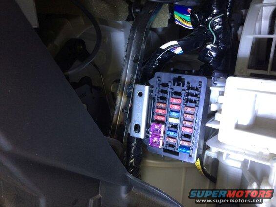 Vehicle fuse box with multiple colored fuses visible.