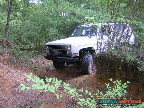 White SUV with aftermarket bumper driving on a dirt trail through woods