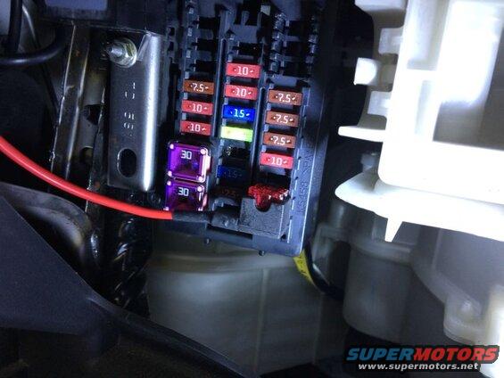 Close-up of a car fuse box with red wire