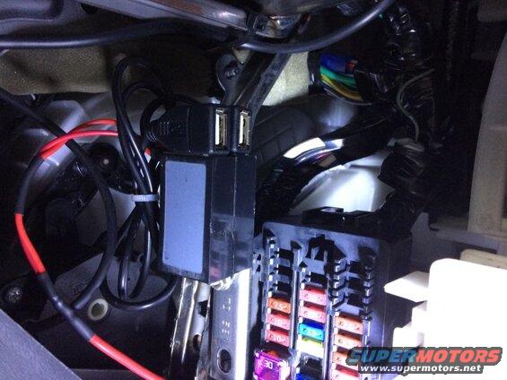 Vehicle interior showing a fuse box and dual USB adapter with wiring.