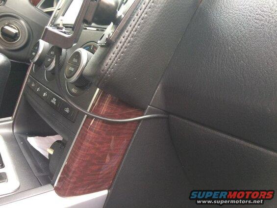 Car dashboard with climate control knobs and wood trim, showing a black cable.