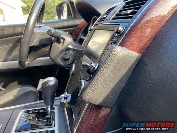 Car interior with phone mount, gear shifter, steering wheel, and wood trim.