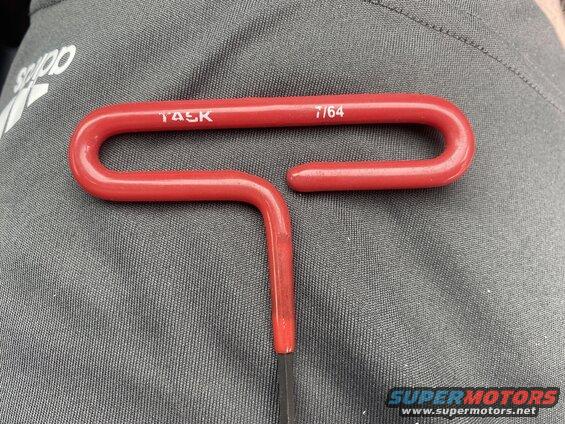 Red T-handle hex wrench with TASK and 7/64 markings on gray fabric.