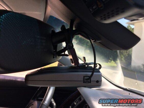 Gray radar detector mounted below a car's rearview mirror.