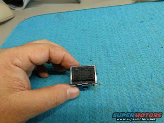 Hand holding a small black electronic component with a textured surface.