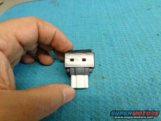 Hand holding a small electronic component with two square openings and a white connector.