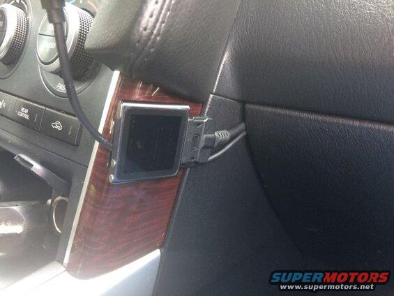 Black electronic device mounted on a car dashboard with wood grain trim.