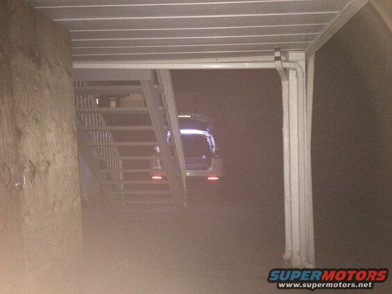 White SUV with open trunk and illuminated taillights parked at night in front of stairs.