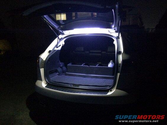 White SUV rear hatch open at night, showing cargo area with black liner and white bottle.