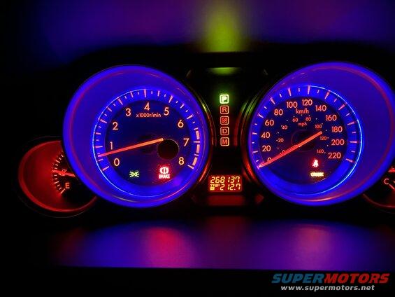 Car dashboard with illuminated speedometer, tachometer, and digital display.